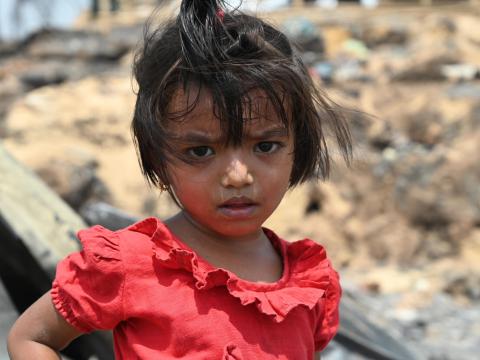 Rohingya girl in a red dress against rubble