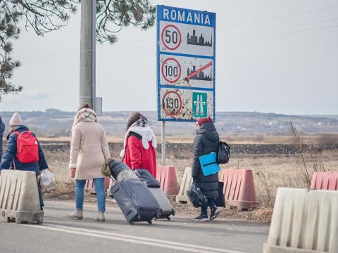 Women, refugees from Ukraine, walk across the boarder into Romania pulling their suitcases.