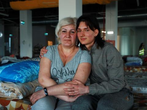 Evhen and his mother sit on a cot bed in a refugee center