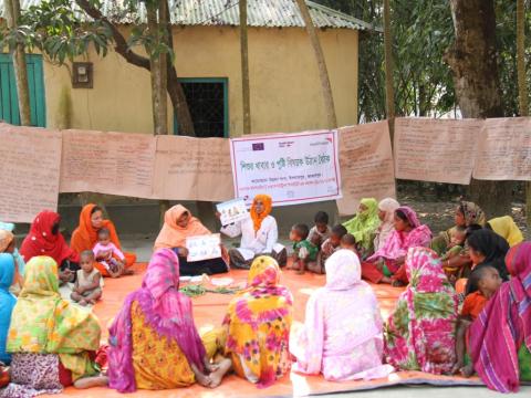 Women sitting in a circle outside listening to a speaker