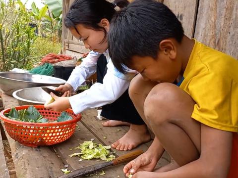 children prepare food on the floor outside their house