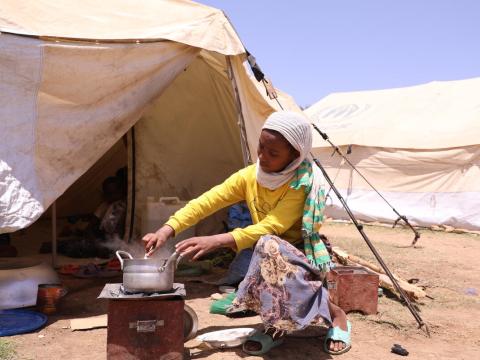 girl sits outside tent mixing food in a pot