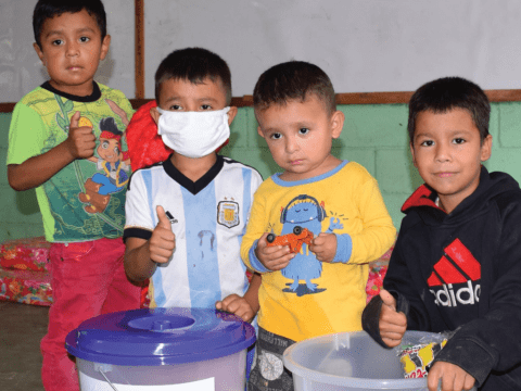 four boys sit in front of containers and show thumbs up for the camera 