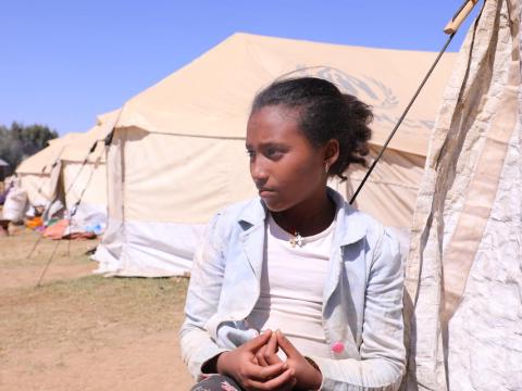a young girl stands outside the refugee tent she lives in