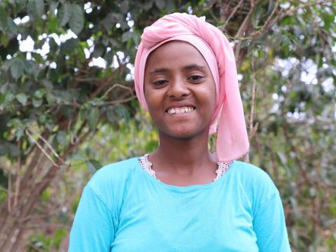 Semira smils for the camera wearing a blue shirt and pink head scarf