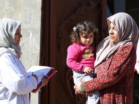 woman speaks to another woman holding a child during a door to door healthcare call