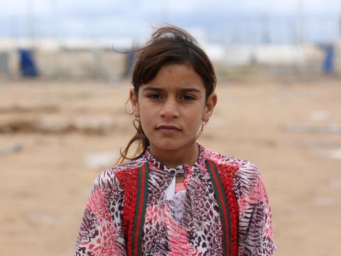 a young girl stands outside a refugee camp