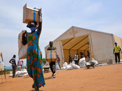 people carry boxes from food distribution tent