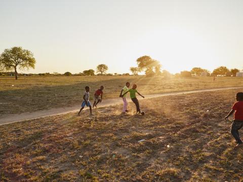 children play futbol in a dirt field