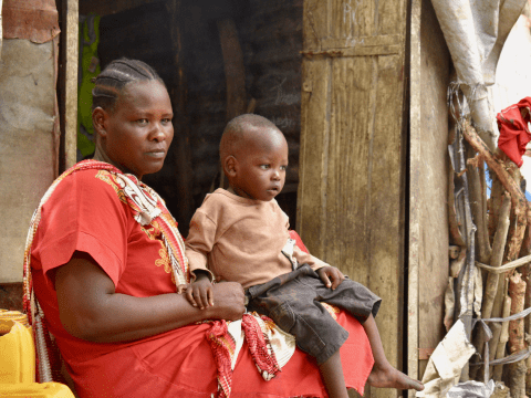 Angelina sits outside her hut with a child on her lap