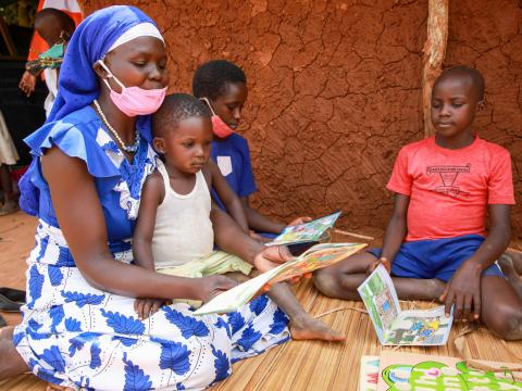 A parent at Mukama Mulungi Community Literacy Centre reads with children as part of assessing and strengthening classroom environment and systems.