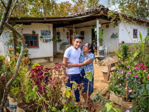 Mother of sponsored child stands in front of their home with her son