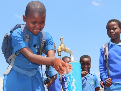 Children in eswatini washing under a tap