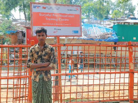 a boy standing against a fence with a signboard