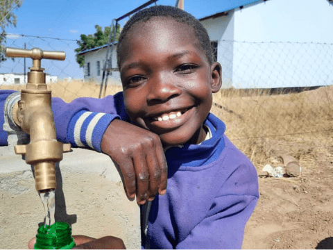 Langelihle Ndlovu gets water from a tap at Dukwe Primary School after the construction of a piped water scheme