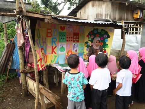 Asnairah, a World Vision trained community volunteer, conducts a teaching session in a small community meeting place, a “Basa Kubo”.
