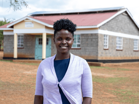 Empowered and Unbroken: Dominica Chelatan stands outside the school where she found refuge from FGM. 