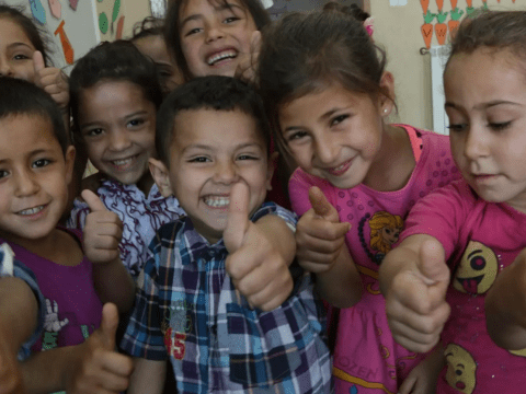 A group of kids smile with their thumbs up.