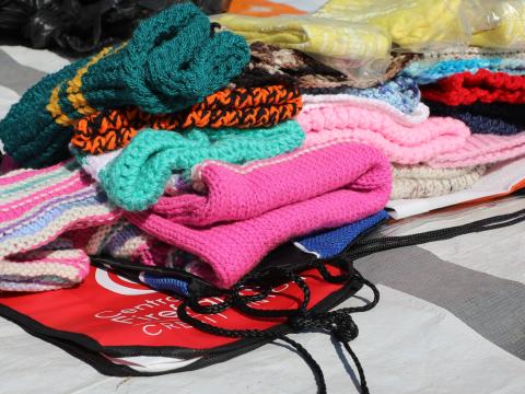 Stack of colorful woolen clothes including jerseys, hats, socks, and scarves, prepared for distribution to children under five in Tuke Village.