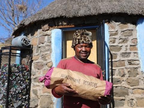 Tseliso stands holding a large bag of freshly harvested potatoes, prepared for the market, symbolizing his journey of empowerment and success.