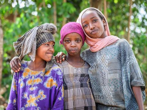 Three girls from Ethiopia smile at the camera with their arms around each other.
