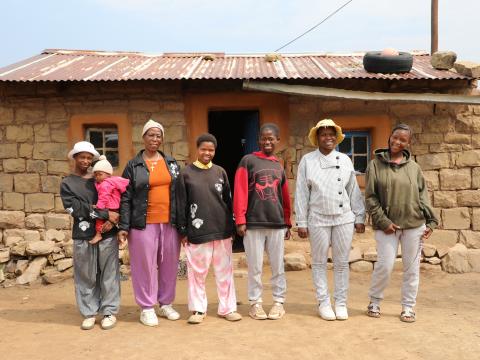 Maletsepileng and her daughters standing together in their new winter clothes, smiling and enjoying warmth and comfort.