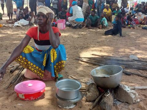 A woman sits close to a fireplace where meals are prepared.