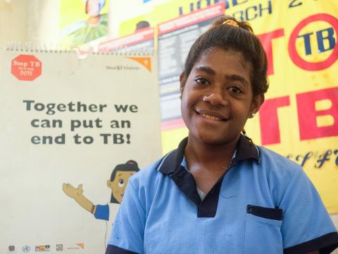 A girls smiles standing in front of tuberculosis poster that reads 'Together we can put an end to TB!'
