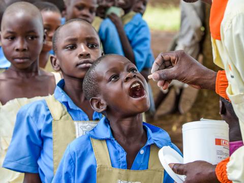 A young child opens her mouth to receive a pill from a World Vision staff