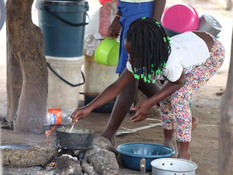 A child in an accommodation center is preparing a meal in a pot that is already half empty for a family with many members.