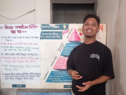 Nahin, a smiling youth leader from World Vision Bangladesh, standing next to educational posters about adolescent rights in Dhaka.