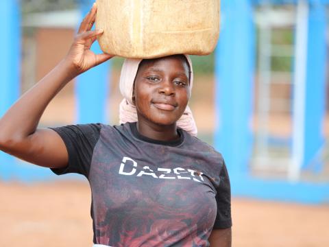 Delina carries a jerrycan, a powerful symbol of safe water now within reach—bringing dignity, relief, and renewed hope closer to home.