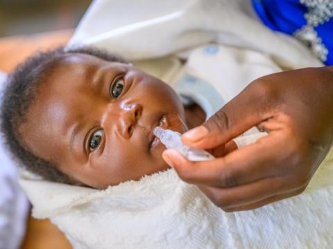 A baby looks into the camera while receiving an oral vaccine in Rwanda