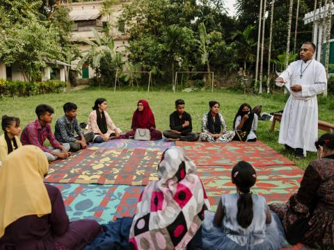 Faith leader speaking to a group of adolescents who are sitting outside