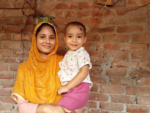 A beaming Sumi holds her young son, Jabelenu, close at their home, embodying the health and hope fostered by the PD/Hearth nutrition program.