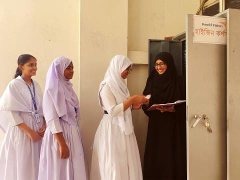 Female students line up at a World Vision hygiene corner in Dhaka school to receive sanitary pads from a teacher.