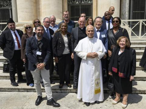 A group of people stand on steps with Pope Leo XIV in white in front