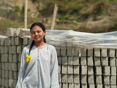 Asta stands in front of rows of bricks stacked by her mother. (© 2026 World Vision International Nepal/Deepshikha Shrestha)