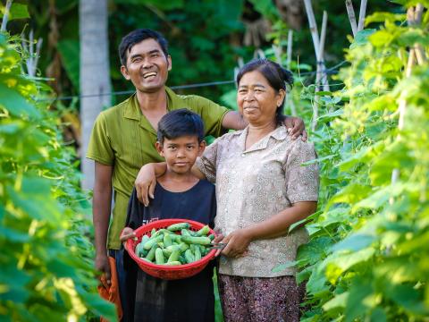 A family stands in a field holding a bowl of crops