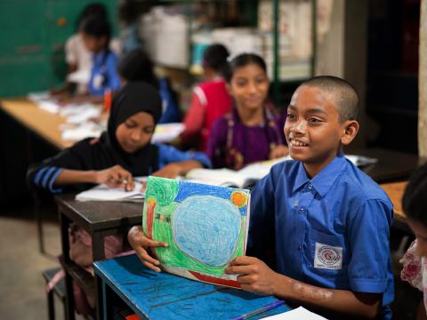 Wearing a crisp blue school uniform, Sipon sits at a desk in his Dhaka classroom, eager and ready to learn.
