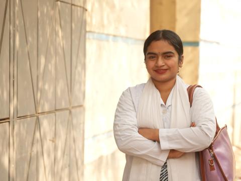 Bhavna stands outside a hospital in her white clinical uniform, smiling as she pursues a career in healthcare after overcoming child marriage.