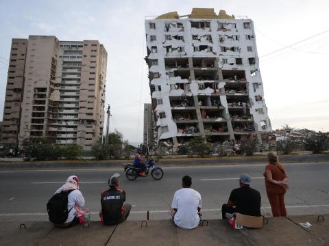 Families sit on the curb in front of apartment buildings that were destroyed by back-to-back earthquakes