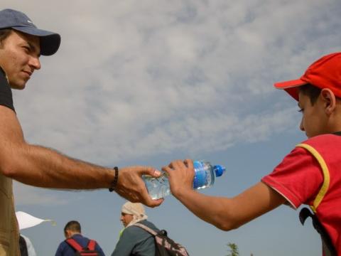 A World Vision staff hands a water bottle to a young man crossing from Serbia into Croatia.