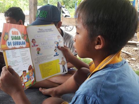 A boy child is reading a book about disaster risk and reduction.