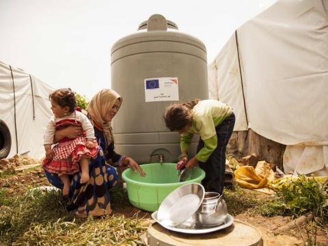 A family wash dishes at a water tank in a informal refugee settlement in Lebanon's Bekaa Valley.