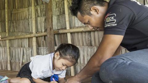 Khmer father helping his daughter with her school work inside their home, Cambodia. Parents involved in child's education