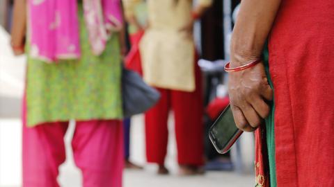 Holding her feature phone with a unique code sent through digital assess transfer platform SIKKA, a recipient waits for her turn to receive ration support in Kathmandu. 