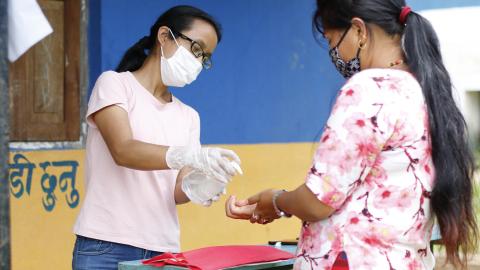 A PNGO staff supports a beneficiary sanitise her hands before receiving hygiene kits for her children. 