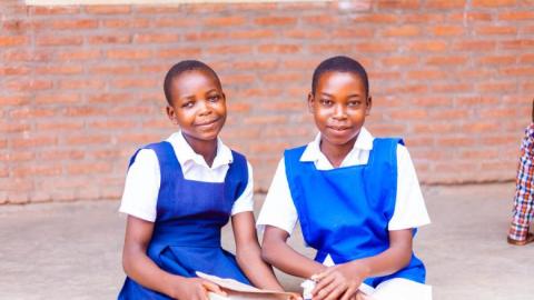 two school girls sit on the steps of their school