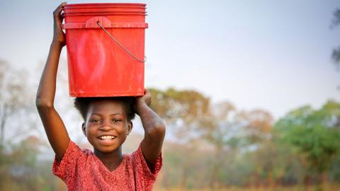 Agnes carrying a bucket of water on her head